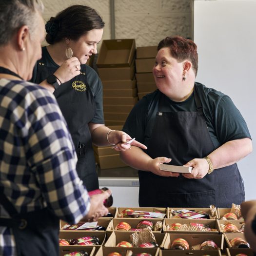 Two women smiling at each other as they pack jars into boxes